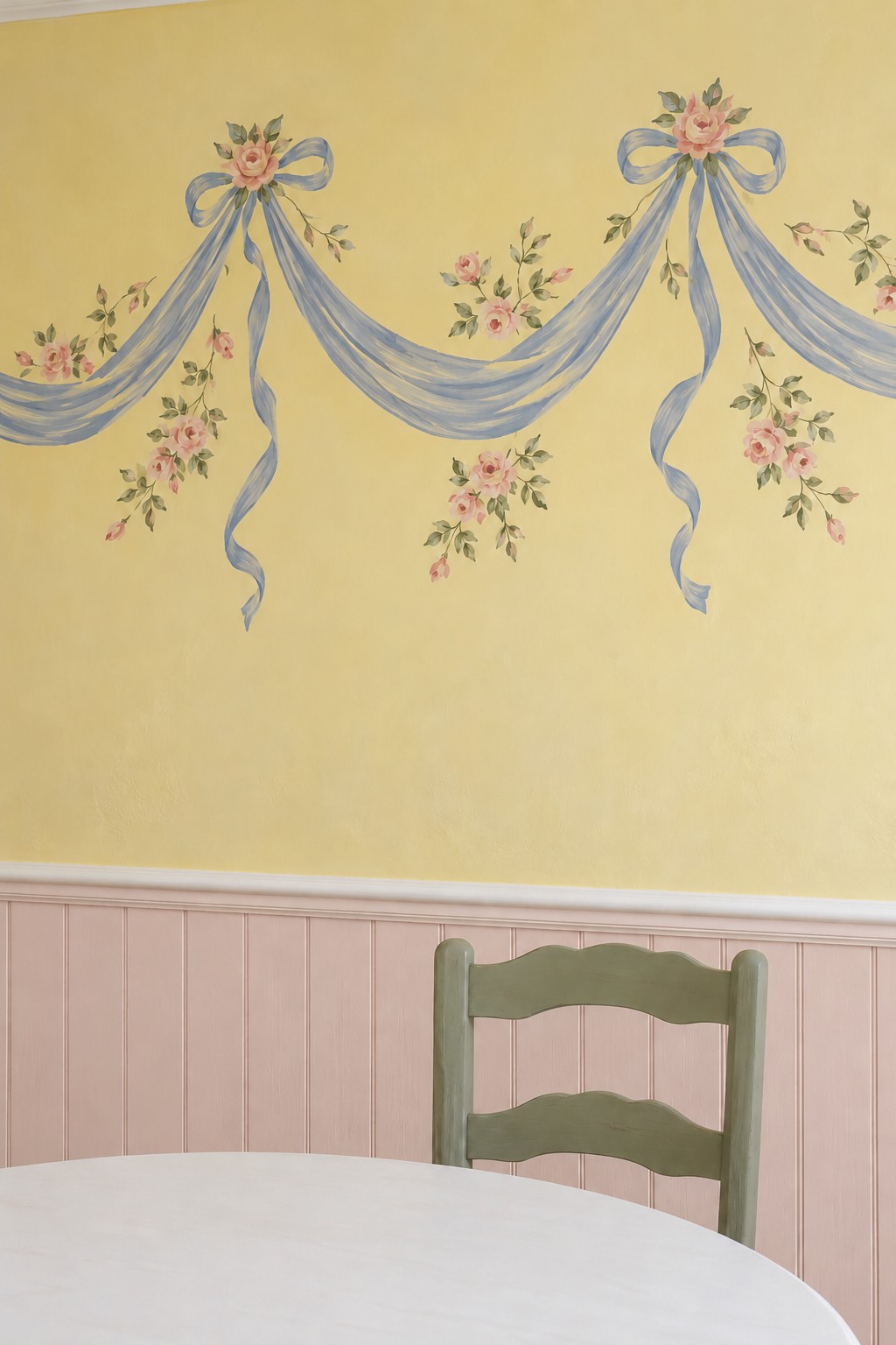 Blue ribbon swags and small pink rose clusters painted across a yellow wall above pink beadboard