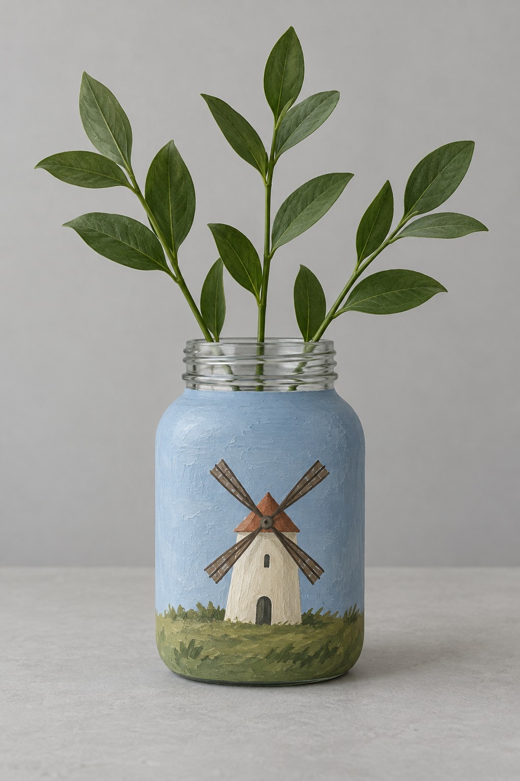 Pale blue jar with a small cream windmill brown sails and painted green grass holding leafy stems