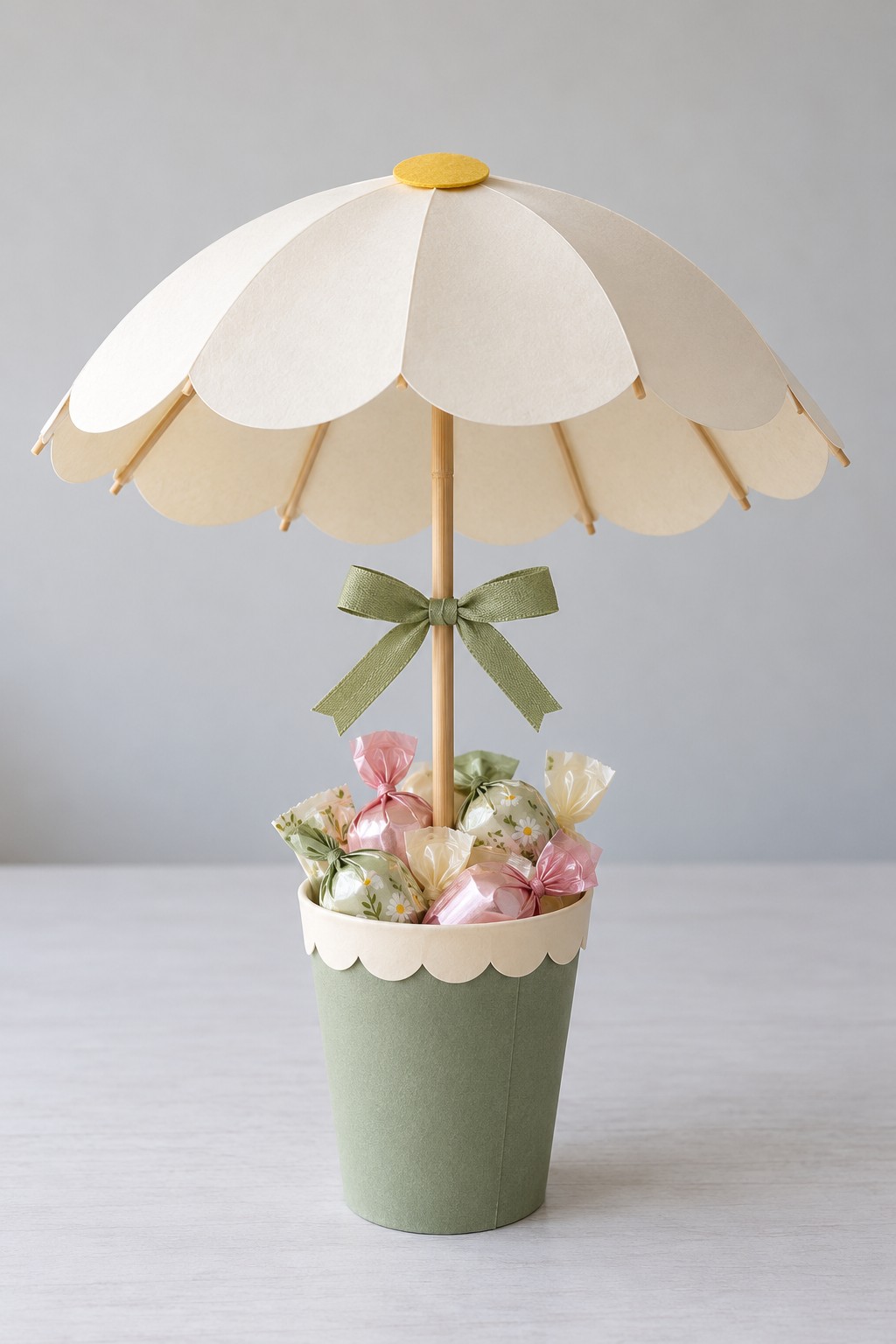 Cream daisy shaped paper parasol over a sage pot filled with pastel wrapped treats