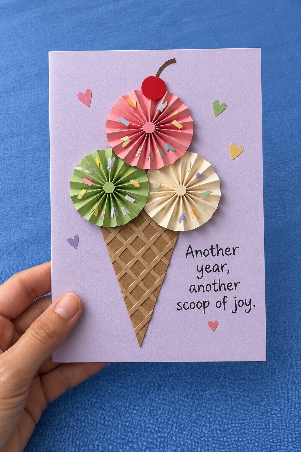 Lavender birthday card with pink, green, and cream paper rosettes arranged above a waffle cone