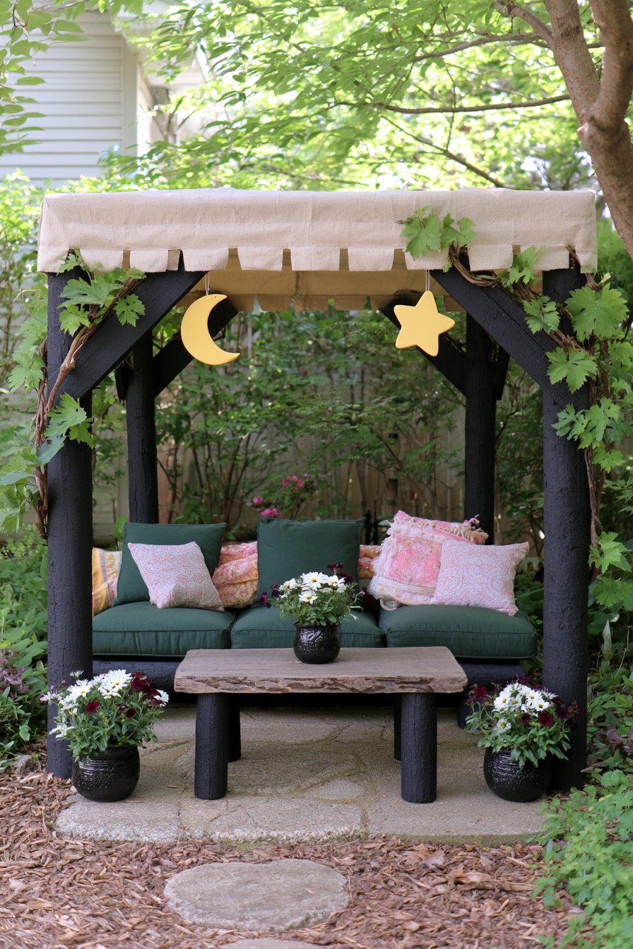 Dark garden frame with a pale canopy, green seating, and yellow moon and star ornaments