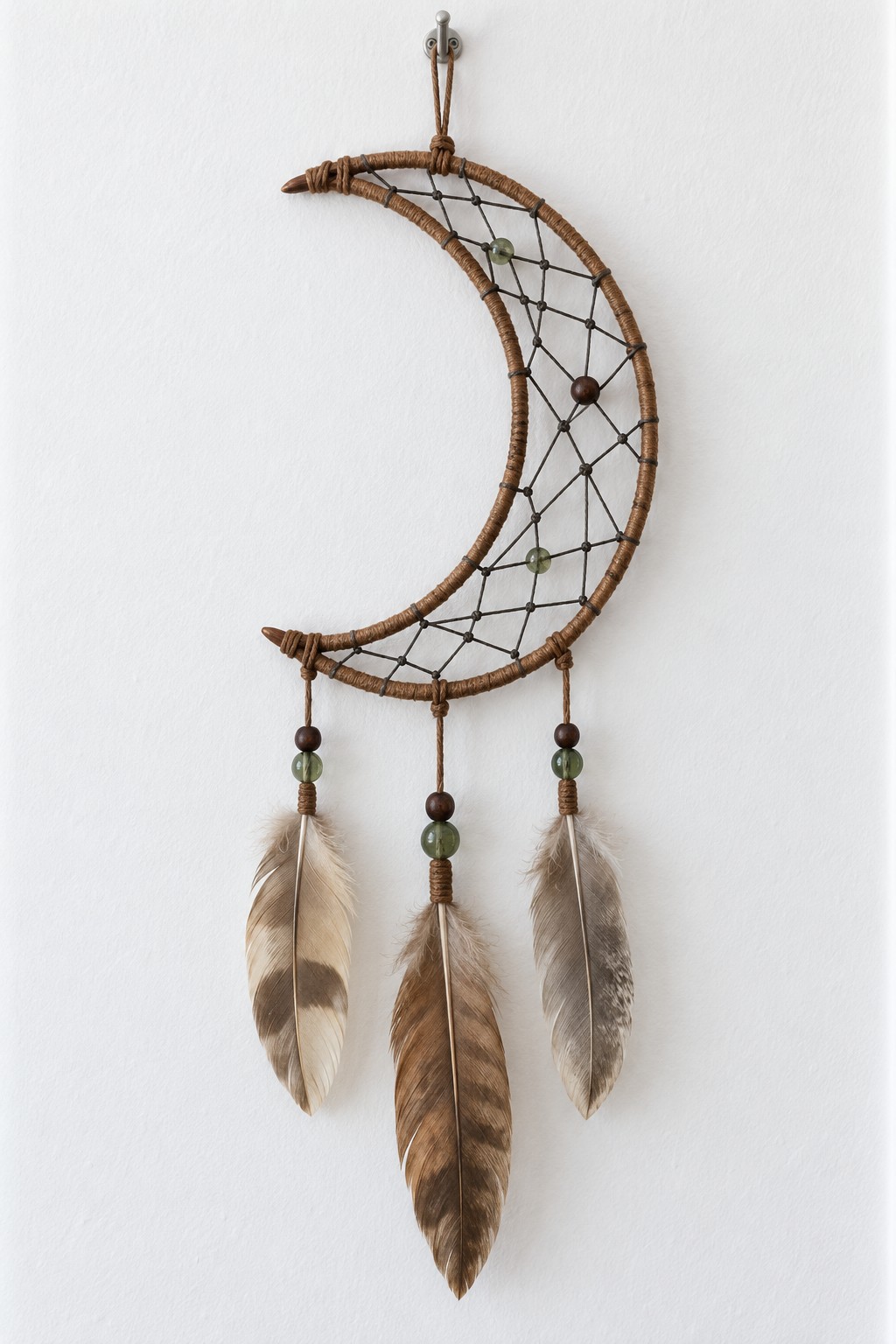 Natural brown crescent frame with a dark cord web, green and wooden beads, and three brown feather pendants