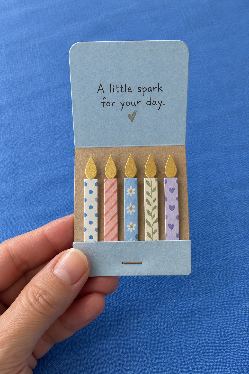 Blue matchbook style card opening to reveal five patterned paper candles with gold flames