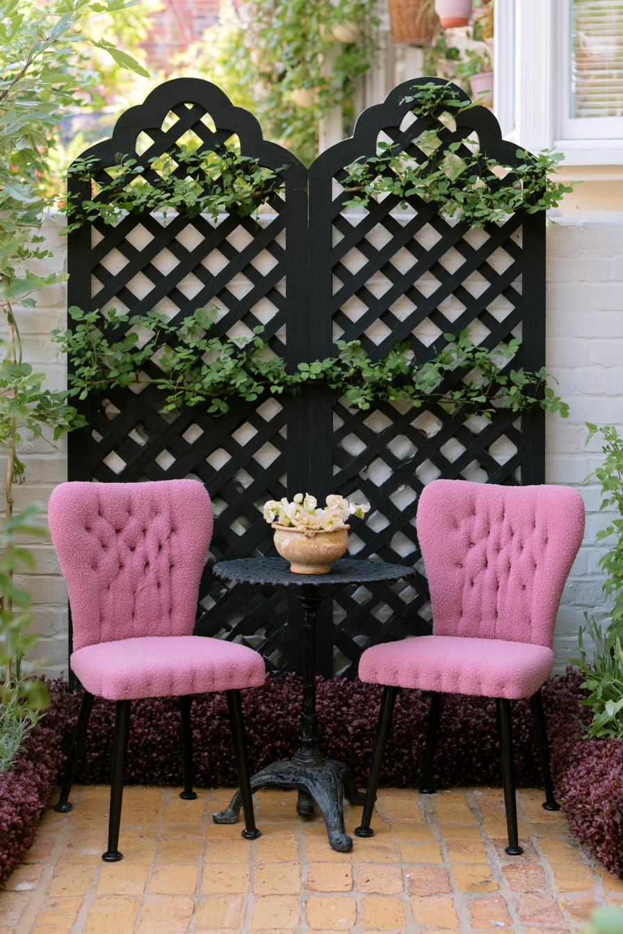 Black lattice panels behind two pink upholstered chairs and a small garden table