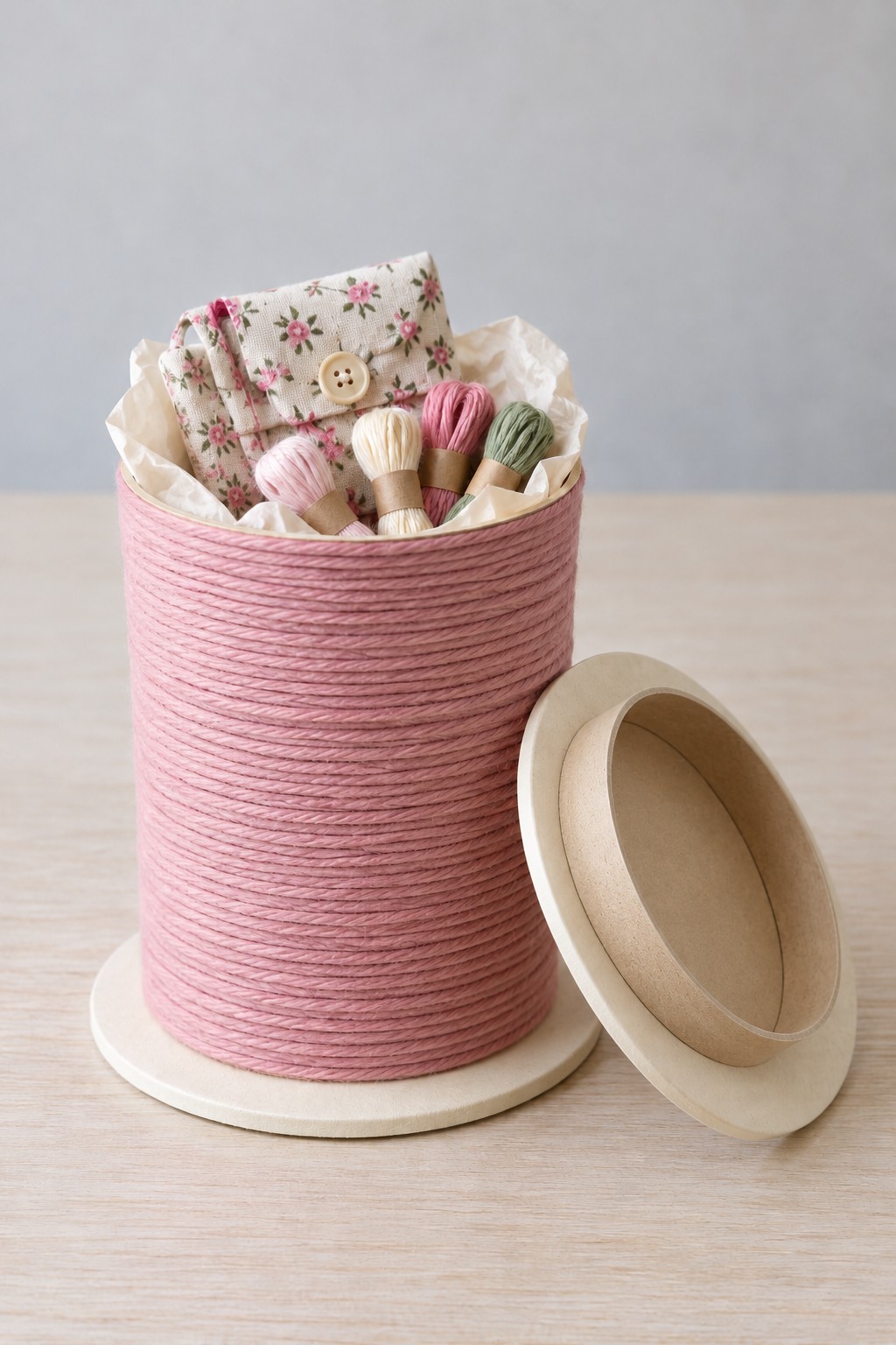 Dusty pink cord wrapped spool shaped canister with a floral fabric pouch and embroidery threads