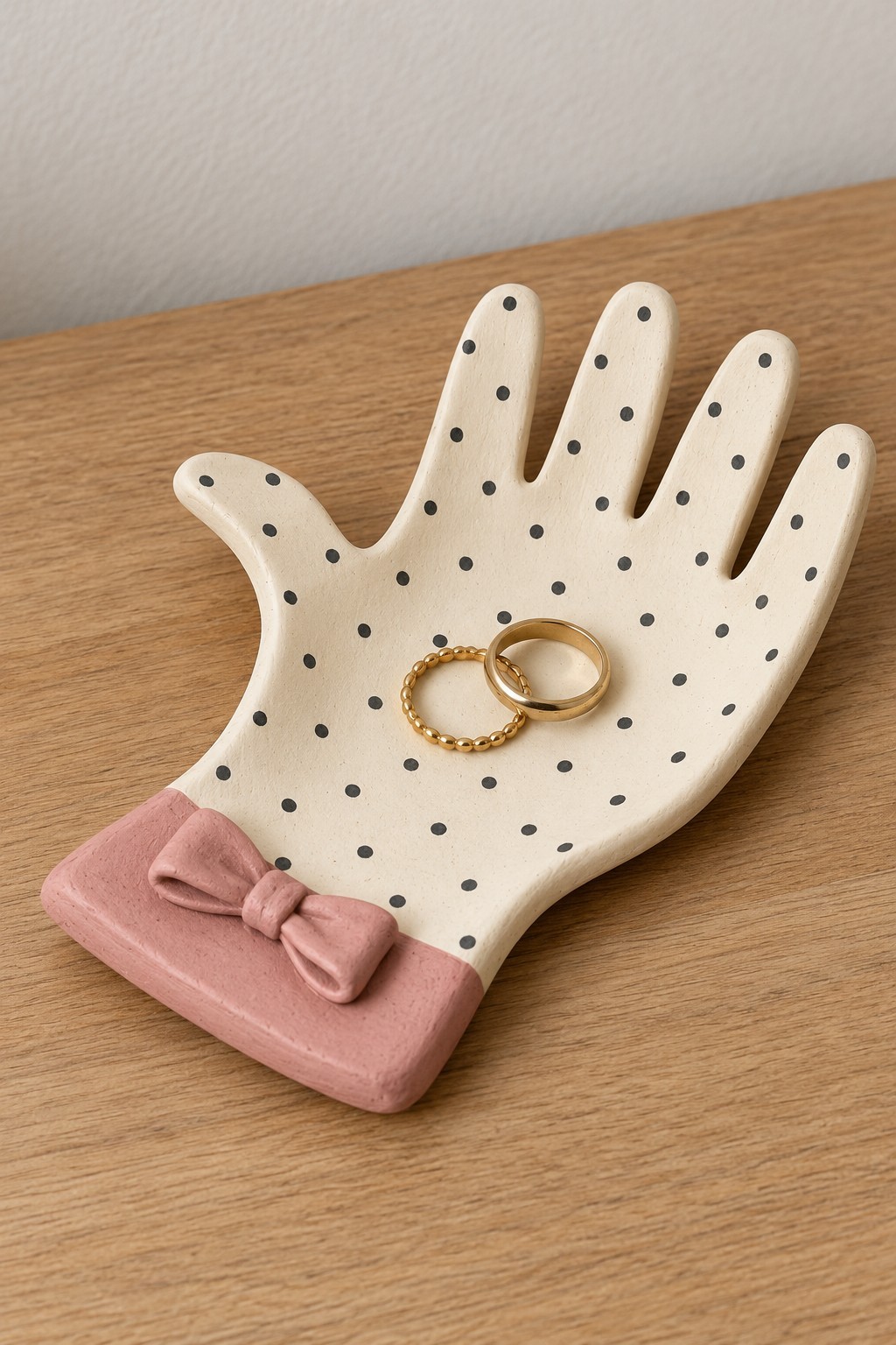Cream hand shaped ring dish with black dots and a pink cuff and bow