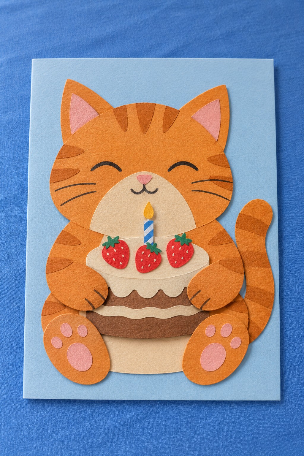 Layered orange cat birthday card holding a strawberry cake on a pale blue background