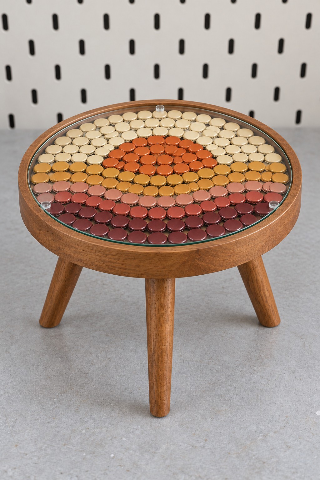 Round wooden side table with a sunset mosaic made from cream, orange, pink, and burgundy metal bottle caps under glass