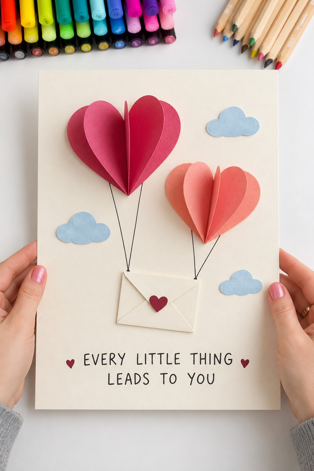 Two dimensional pink and coral heart balloons with blue clouds and drawn strings attached to a tiny cream envelope