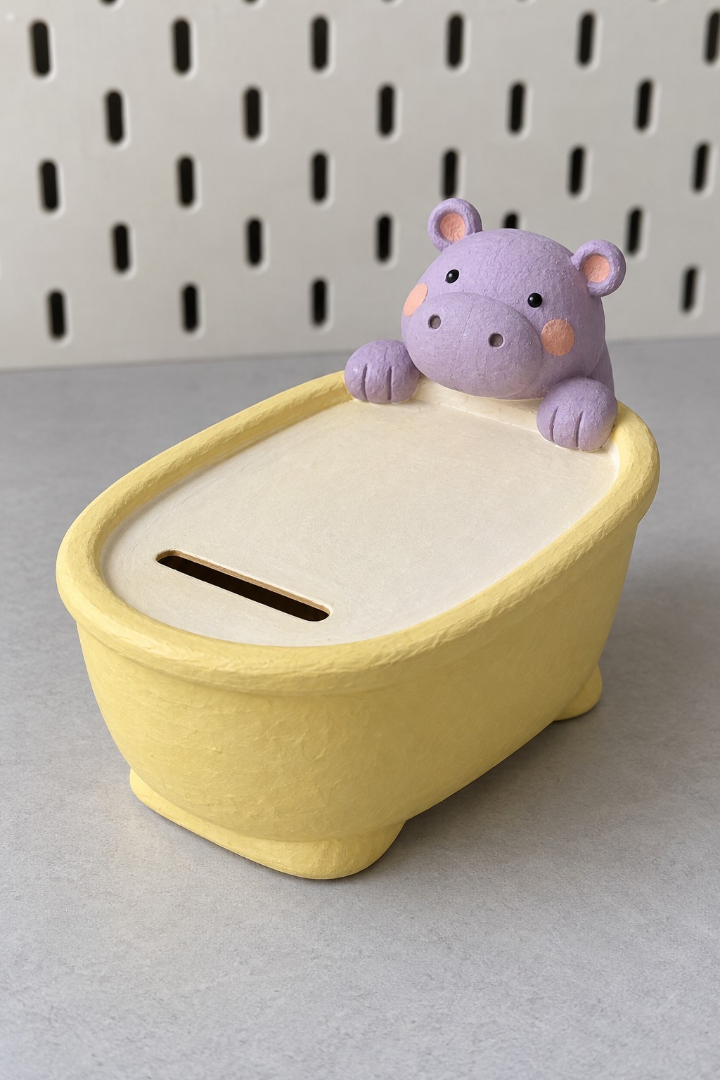 Yellow bathtub shaped coin bank with a cream slotted lid and a purple hippo resting on the rear rim