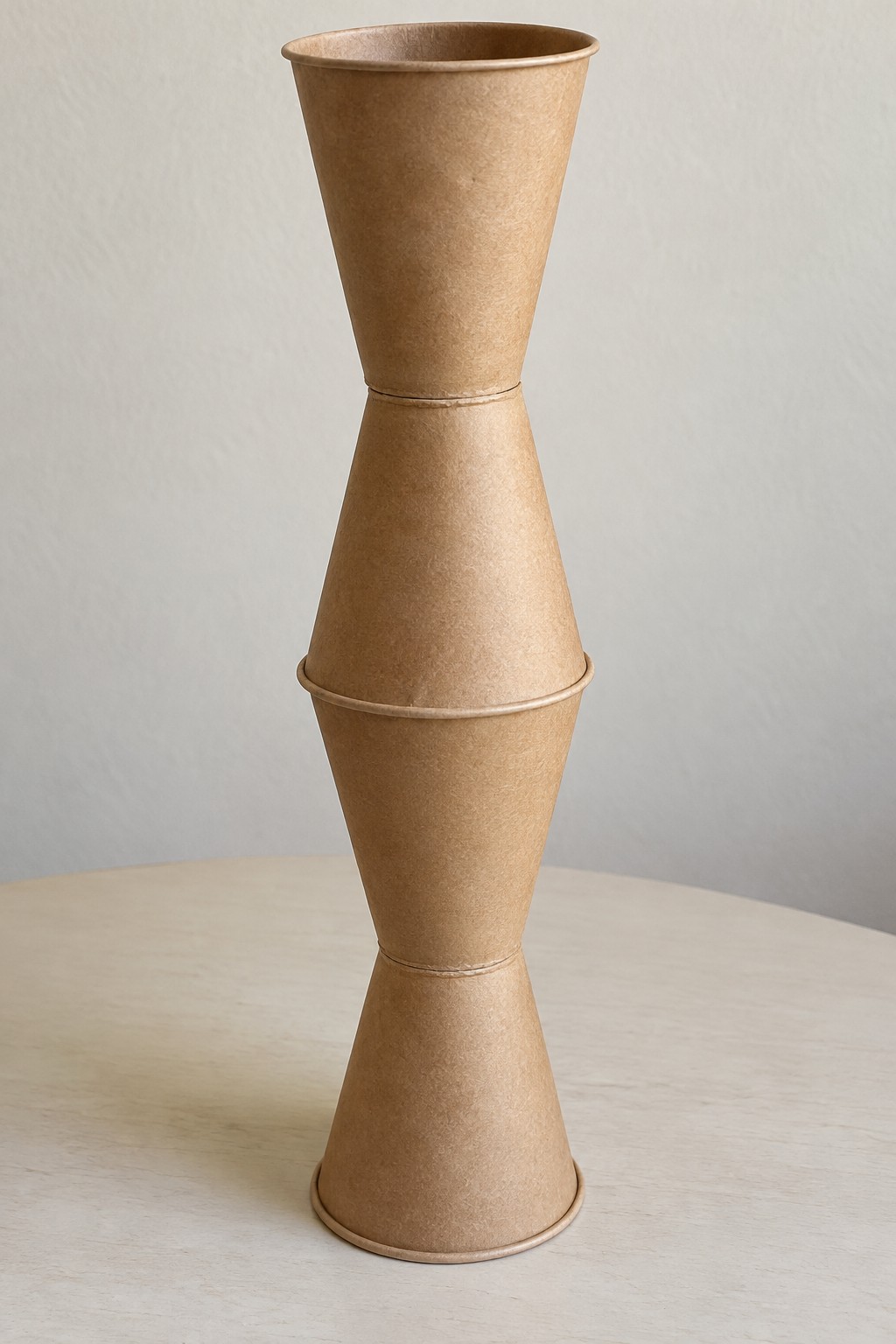 Four natural brown paper cups joined in alternating directions to make a narrow sculptural column