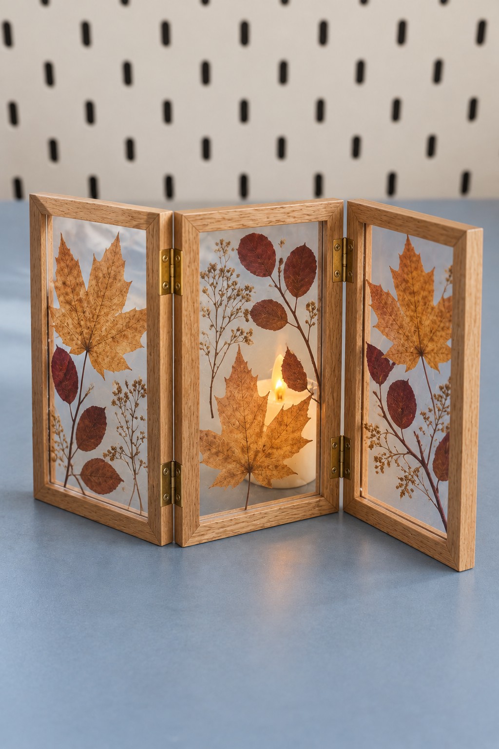 Three hinged wooden botanical panels arranged around a warm battery candle