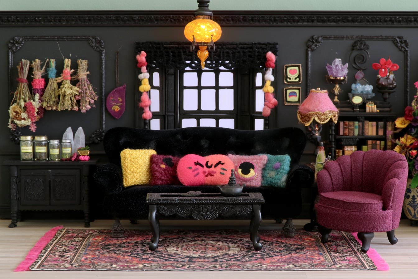 Black paneled parlor with a black sofa, berry armchair, colorful cushions, dried stems, and an ornate coffee table