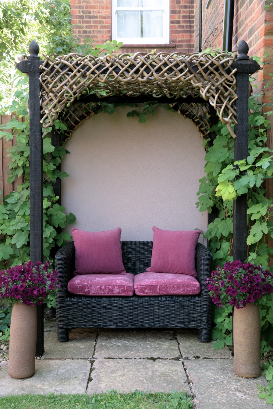 Woven canopy over a dark garden loveseat with pink cushions
