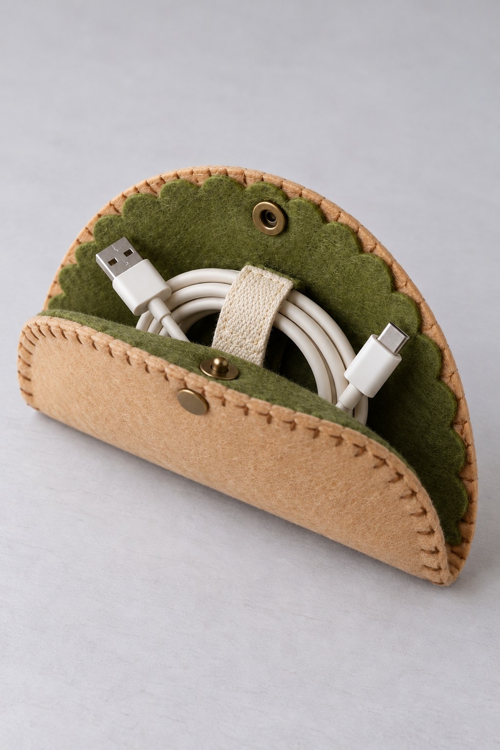 Tan and green felt taco pouch with blanket stitched edges, a press stud, and a charging cable held by a cream loop