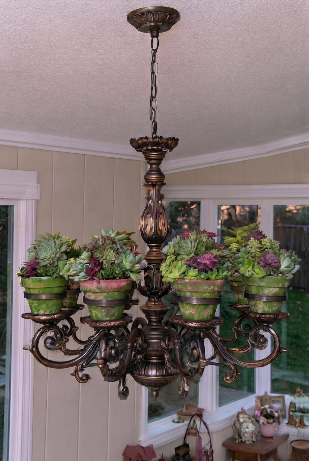 Bronze chandelier holding painted clay pots filled with colorful succulents in a sunroom