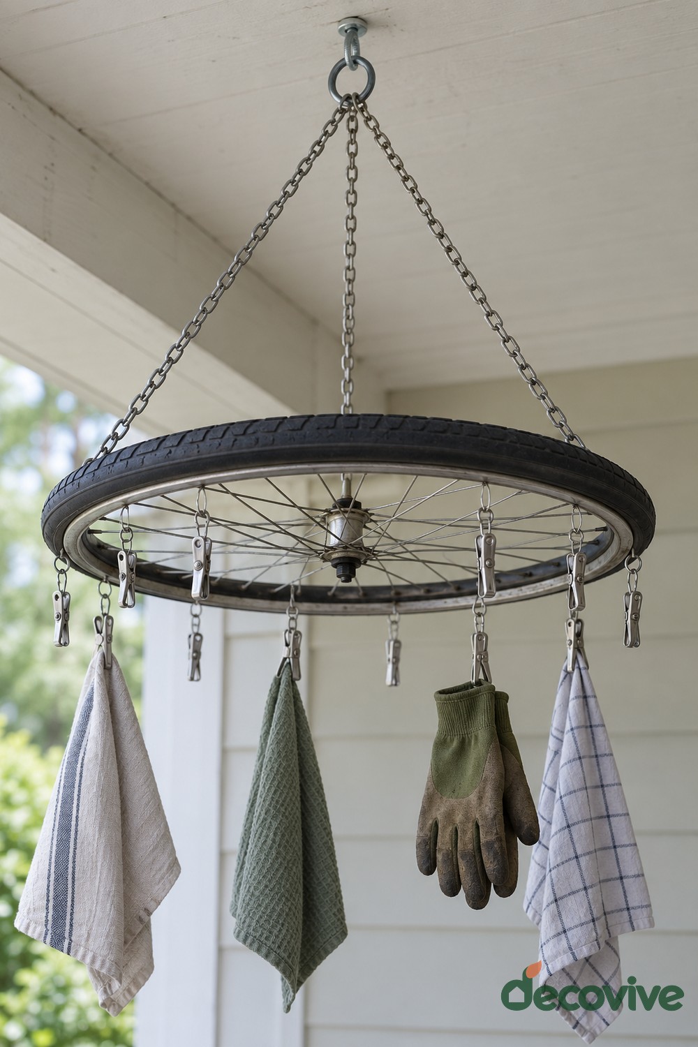 Horizontal bicycle wheel with its black tire suspended by chains and fitted with clips holding cloths and gardening gloves
