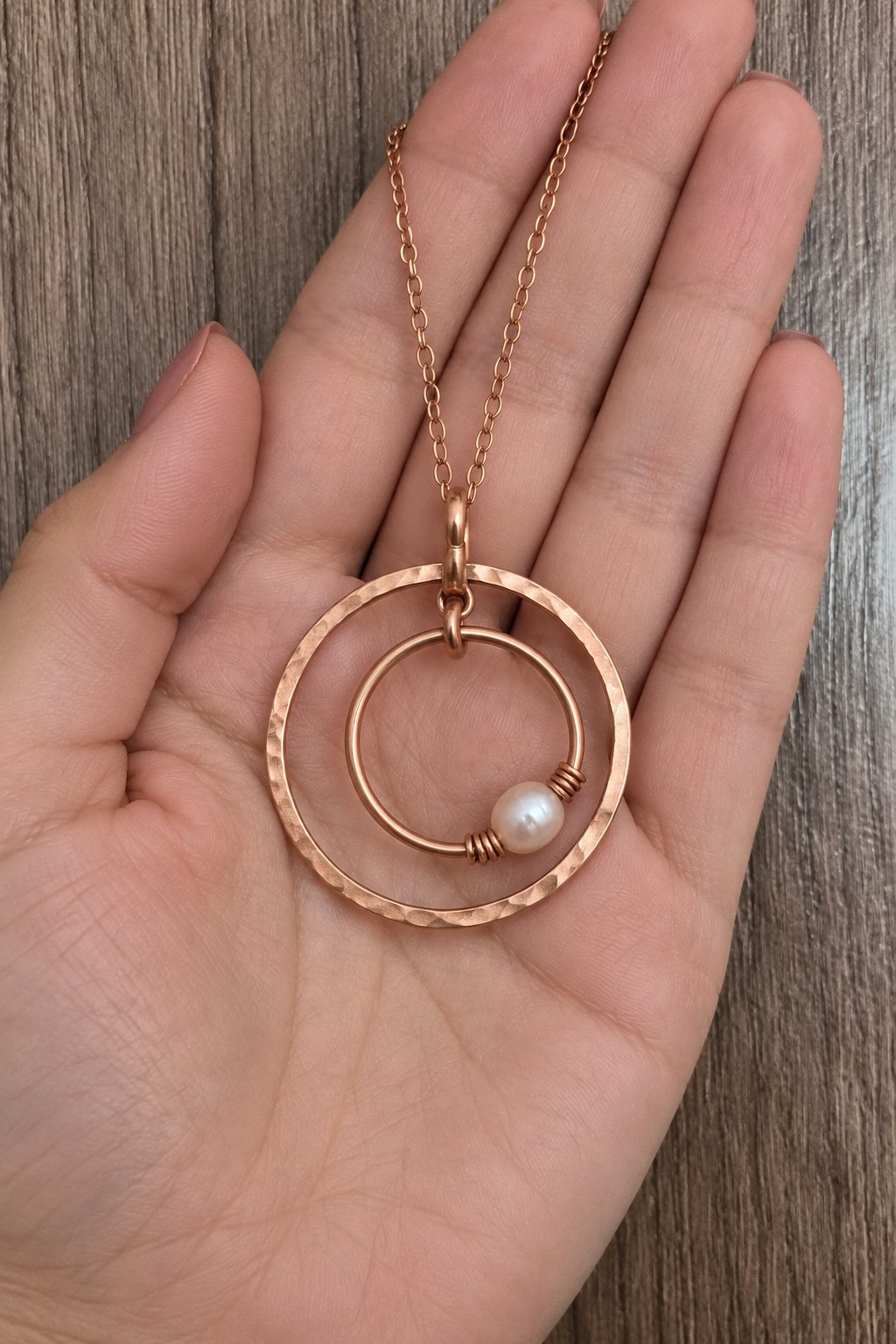 Two nested copper circles with one pale pearl like bead on the smaller inner circle