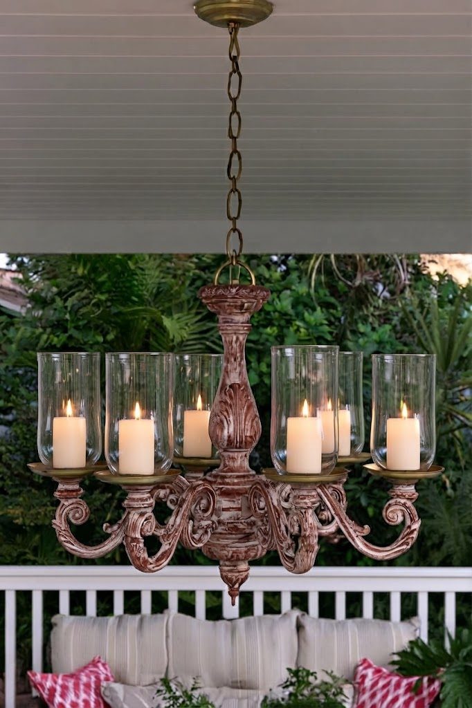 Whitewashed red chandelier with glass hurricane candle holders hanging on a covered porch