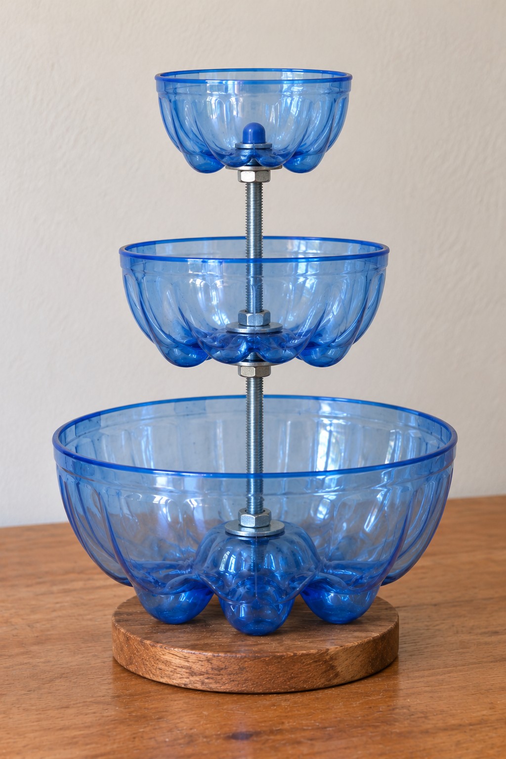 Three blue plastic bottle base bowls supported by washers and nuts on a central threaded rod above a wooden base