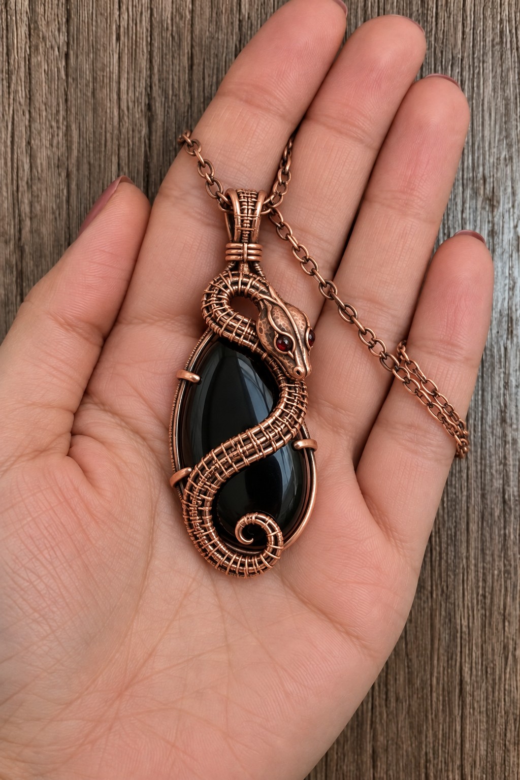 Copper serpent with a woven body curving over a large elongated black cabochon