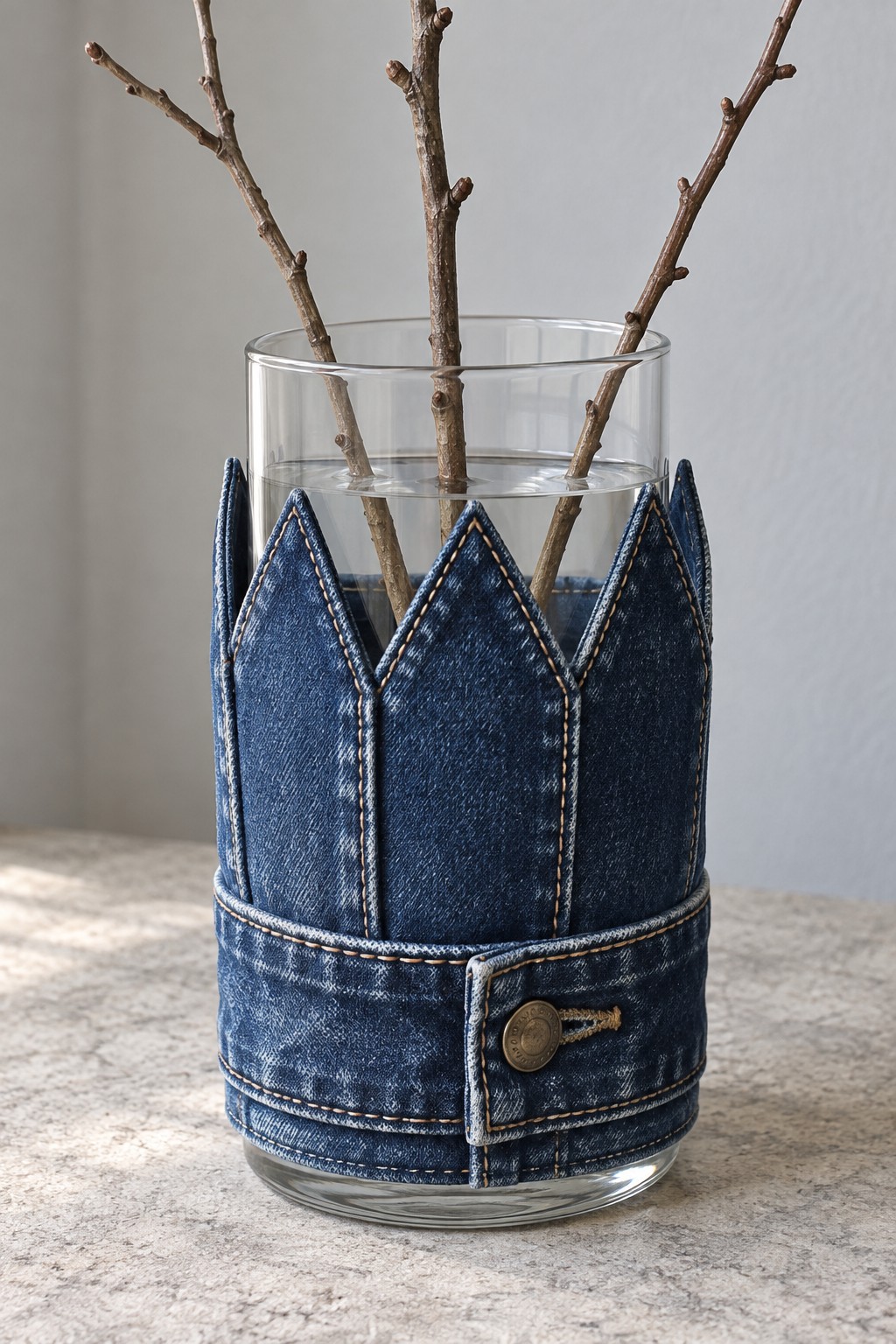 Cylindrical glass vase wrapped in a pointed denim sleeve and a reused waistband
