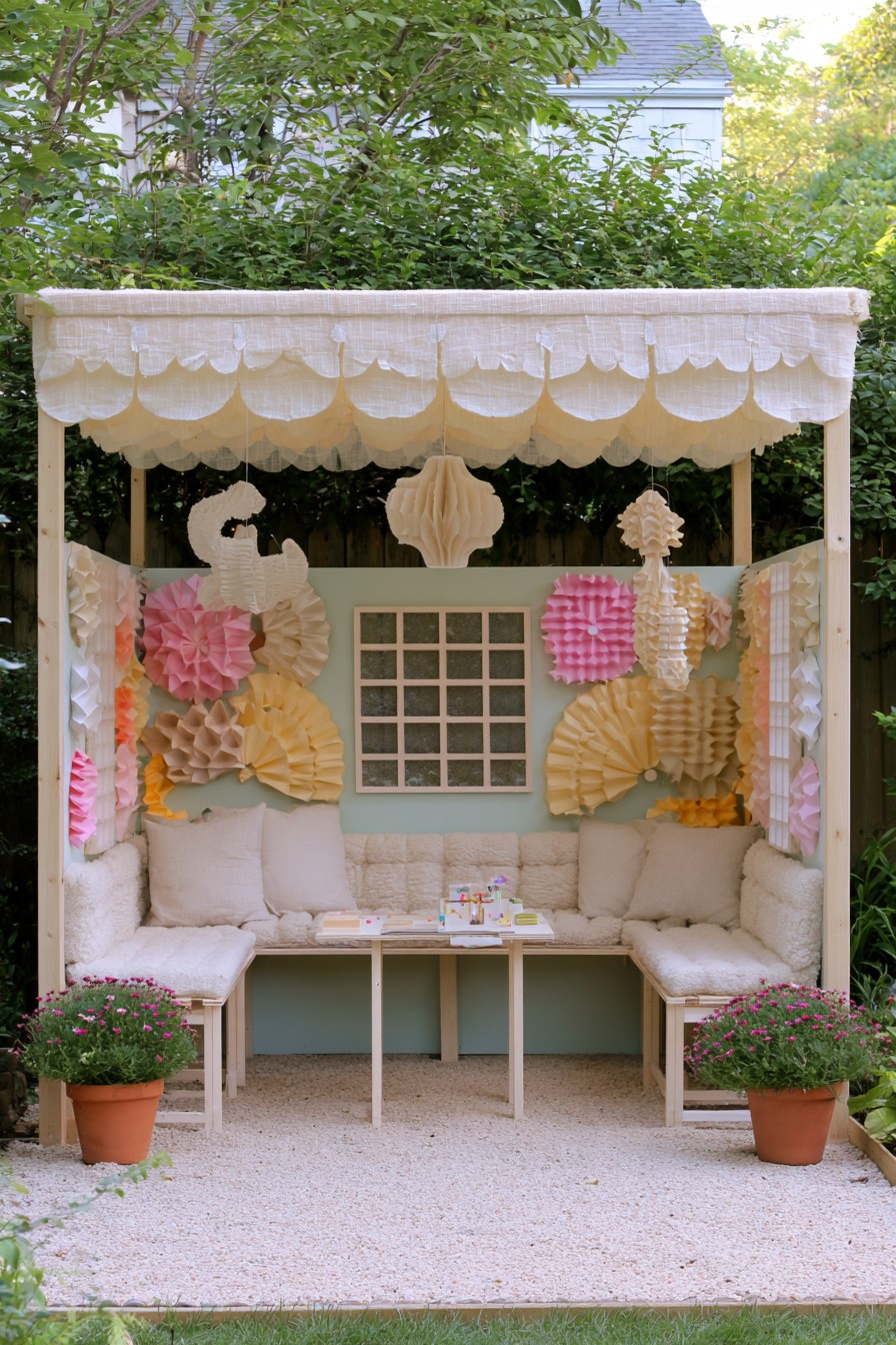 Cream-cushioned benches with pastel paper-like rosettes and fans under a fabric canopy