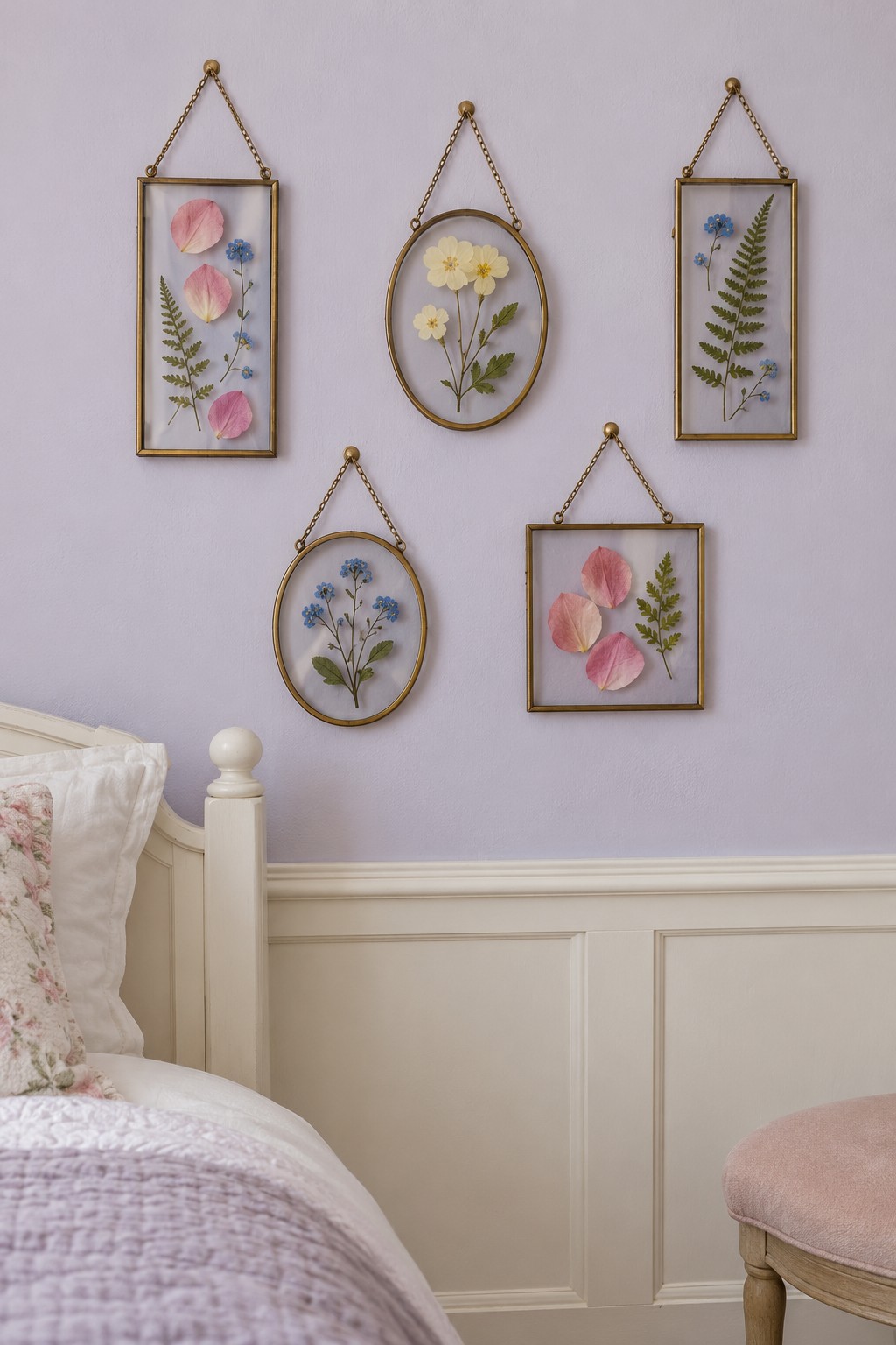 Five small brass hanging frames with pressed flowers and fern leaves on a lilac bedroom wall