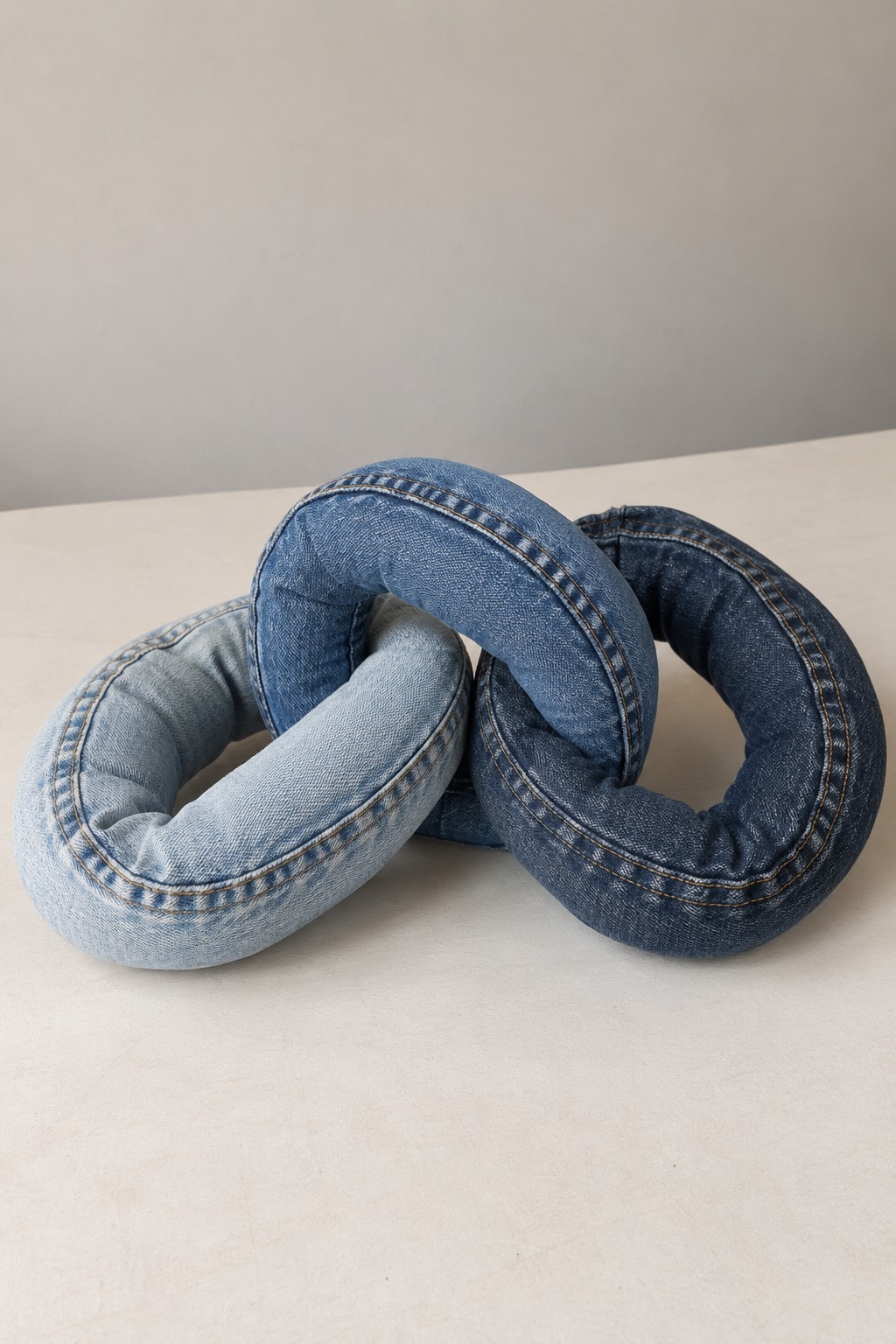 Three softly stuffed interlocking denim rings made from different shades of worn jeans