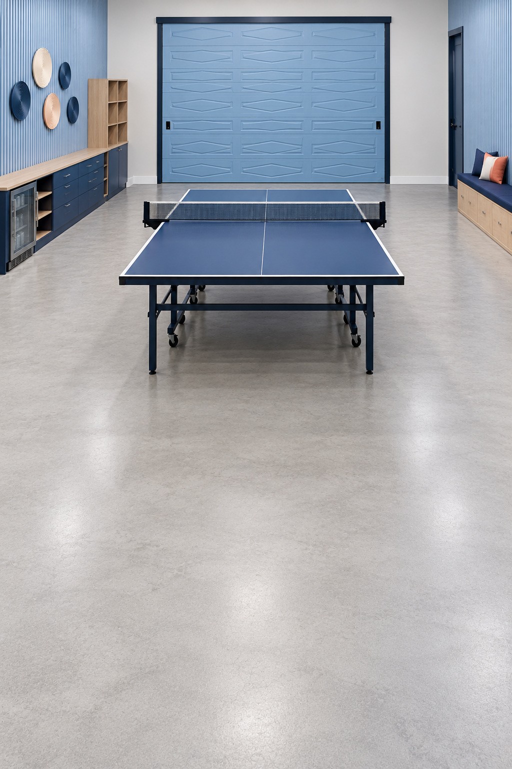 Blue garage table tennis room with a central folding table, shallow blue cabinets, wall bench, and open floor