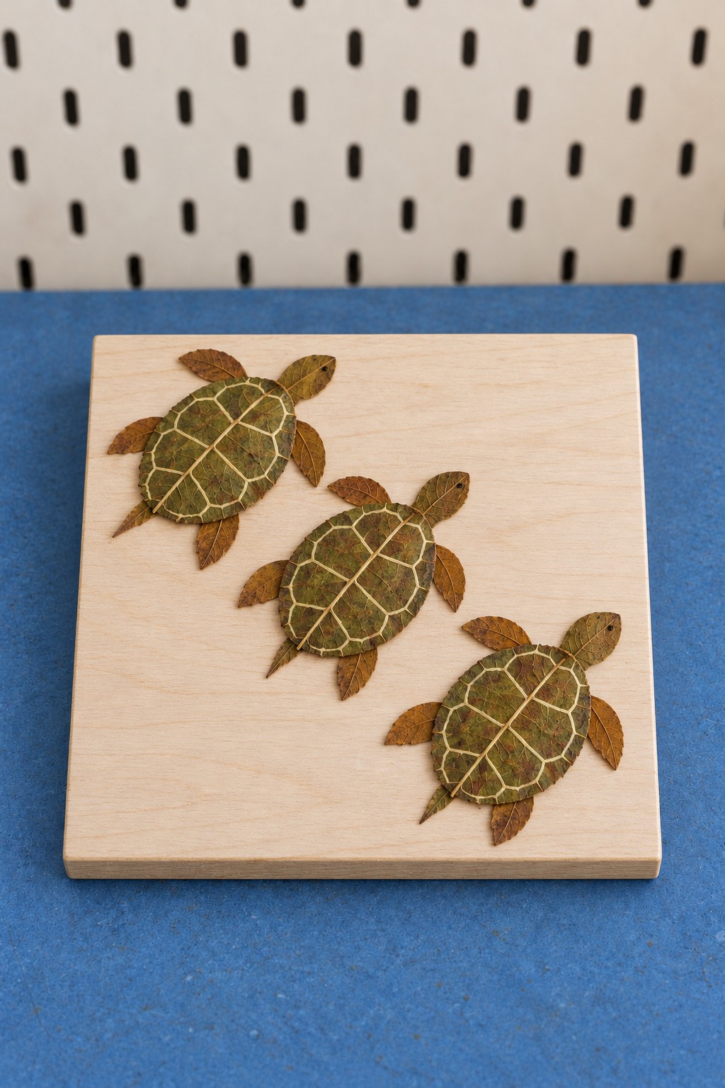 Three green leaf turtles with pale shell markings arranged diagonally on a square wooden plaque