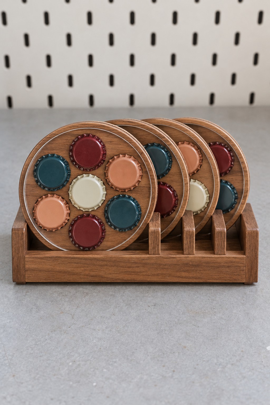 Four round wooden bottle cap coasters with teal, burgundy, peach, and cream caps and clear covers in a wooden rack