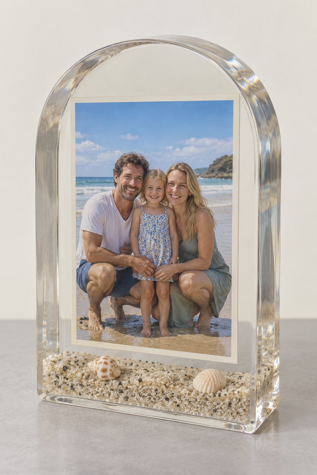Clear arched resin keepsake containing a beach portrait above dry sand and small shells