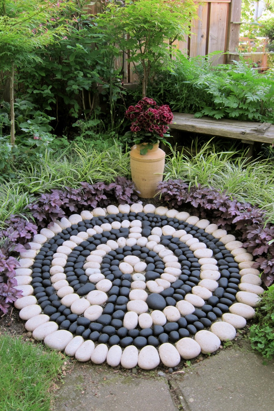 Black and white pebble spiral bordered by purple foliage beside a garden urn