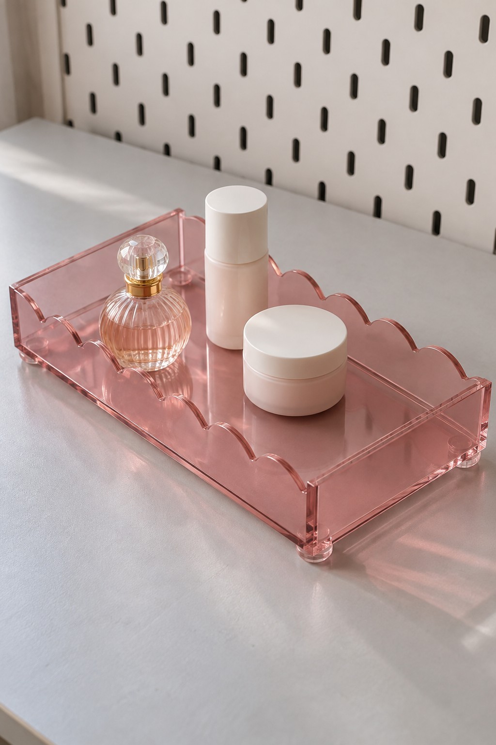 Pink acrylic vanity tray with a scalloped back holding perfume and skin care containers