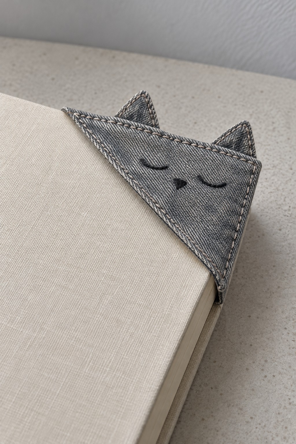 Gray denim triangular cat bookmark fitted over a book page corner