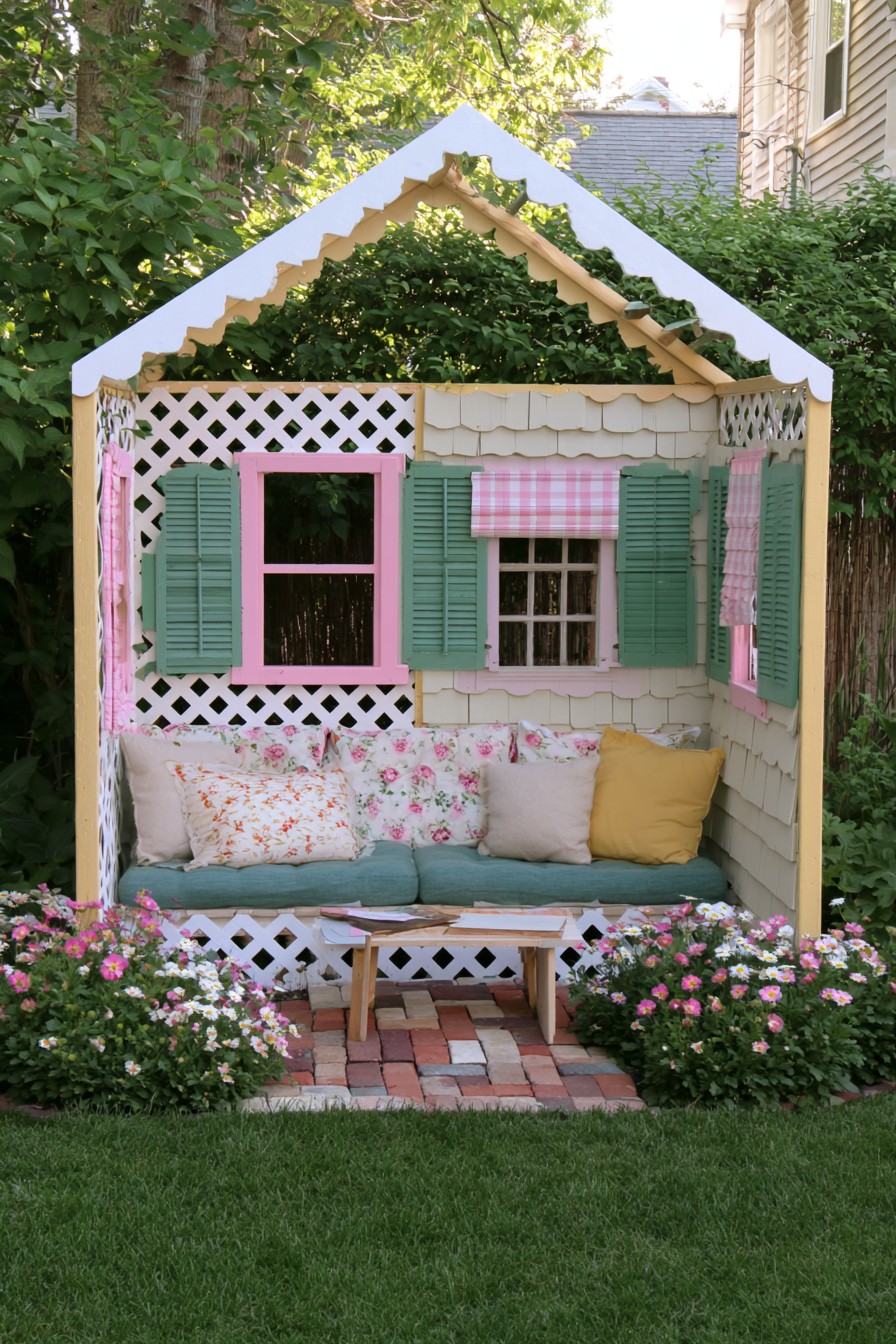 Cottage-style garden seat with white lattice, green shutters, and a teal cushion