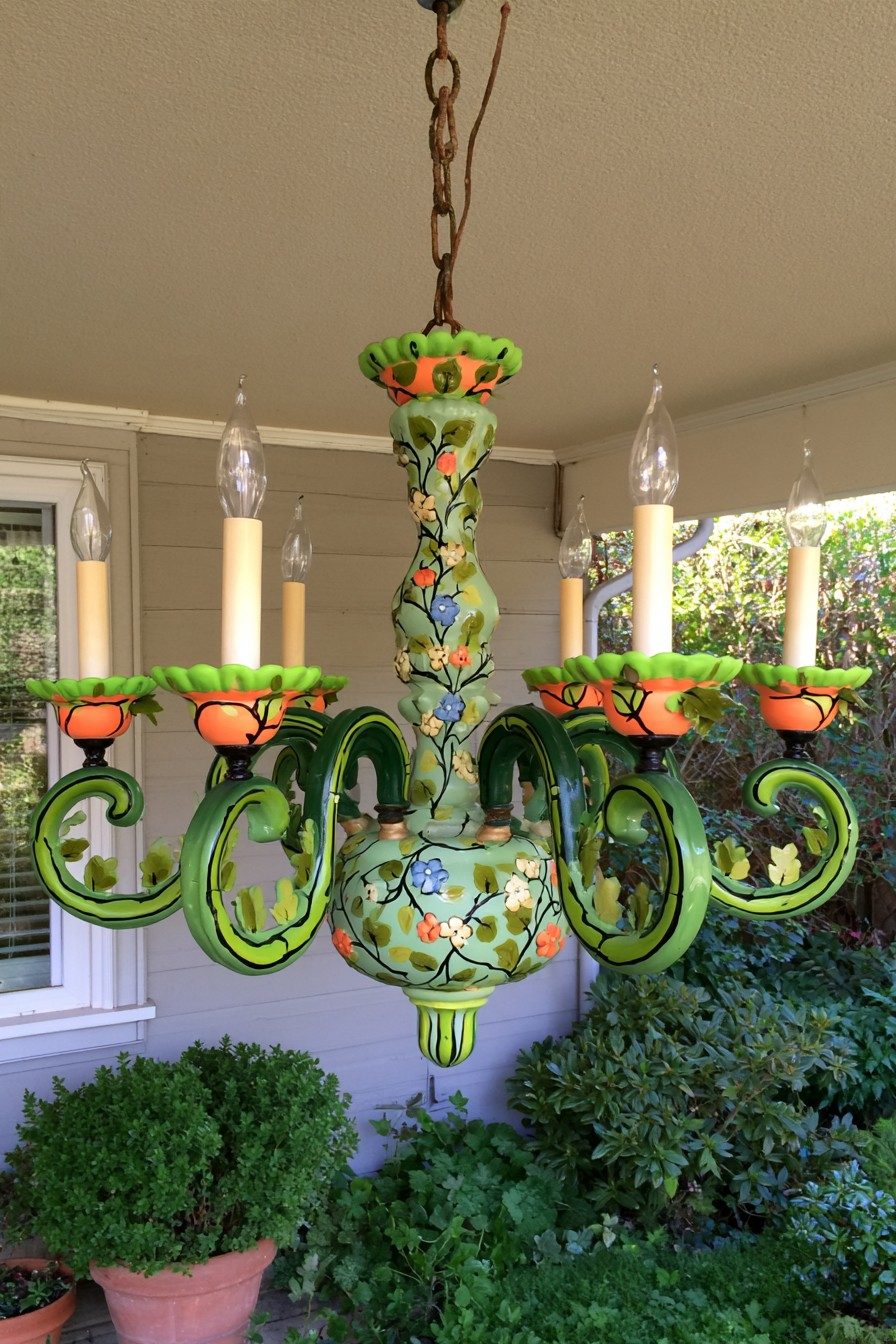 Hand painted chandelier in green with orange cups and small flowers hanging on a porch