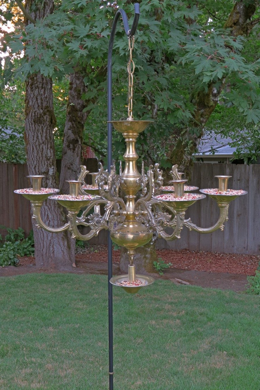 Metal chandelier with open seed dishes hanging from a shepherd's hook in a garden lawn