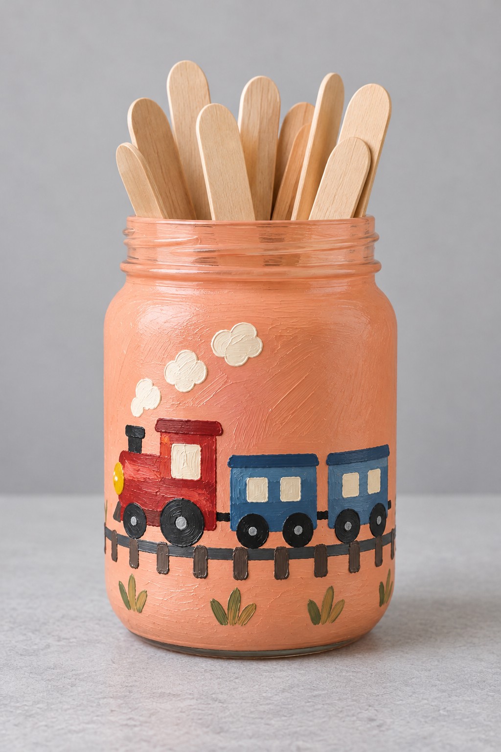 Peach jar with a painted red engine blue carriages black railway track and cream smoke holding wooden sticks
