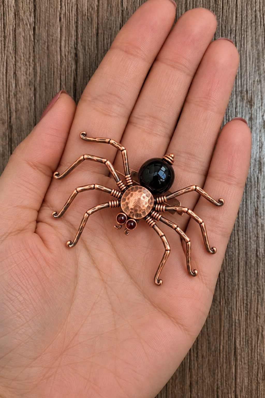Copper spider brooch with eight articulated looking wire legs, a hammered body, and a large dark bead