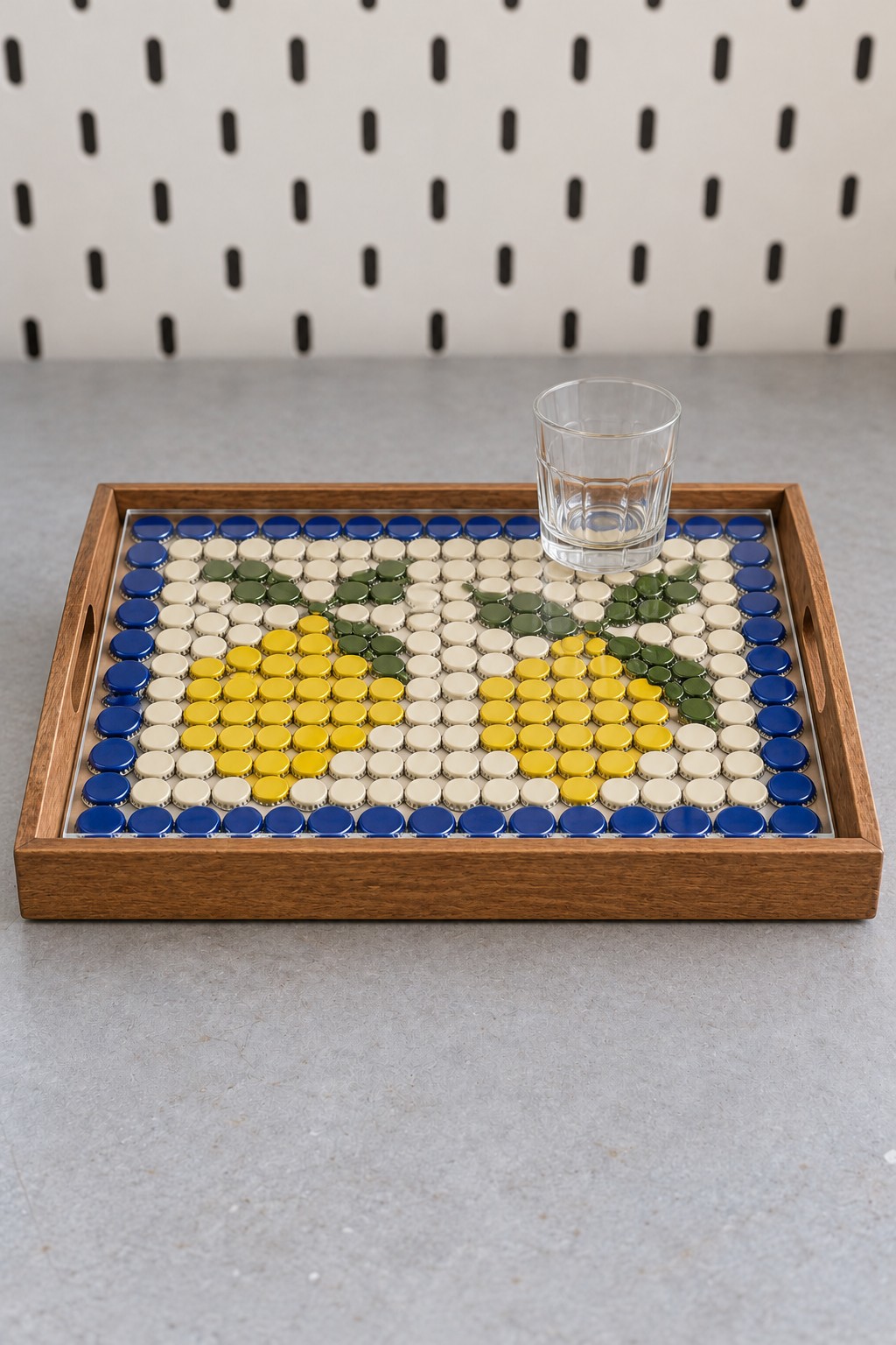 Wooden tray with yellow lemon and green leaf bottle cap mosaic, cream background, and blue border beneath a clear top