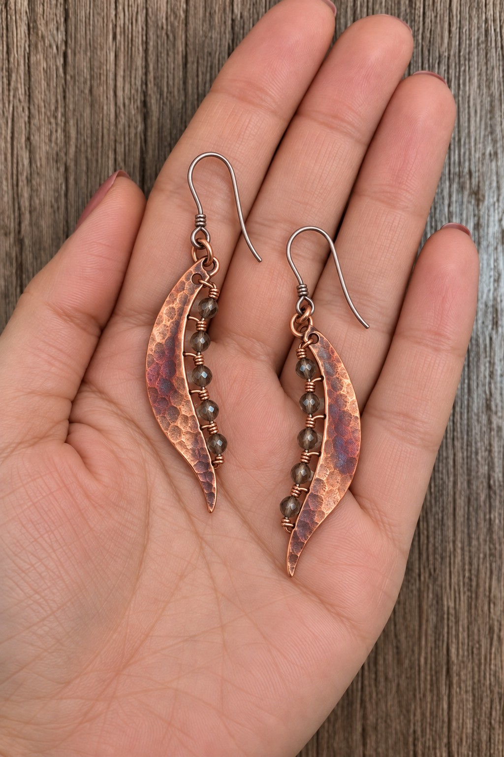 Curved copper leaf earrings with dark green beads following one inner edge