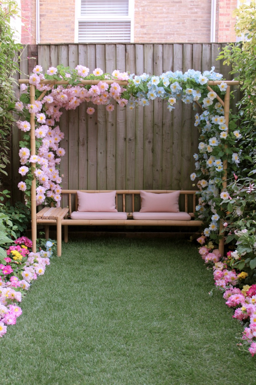 Long cushioned bench beneath an open bamboo arbor with pink and pale blue flowers