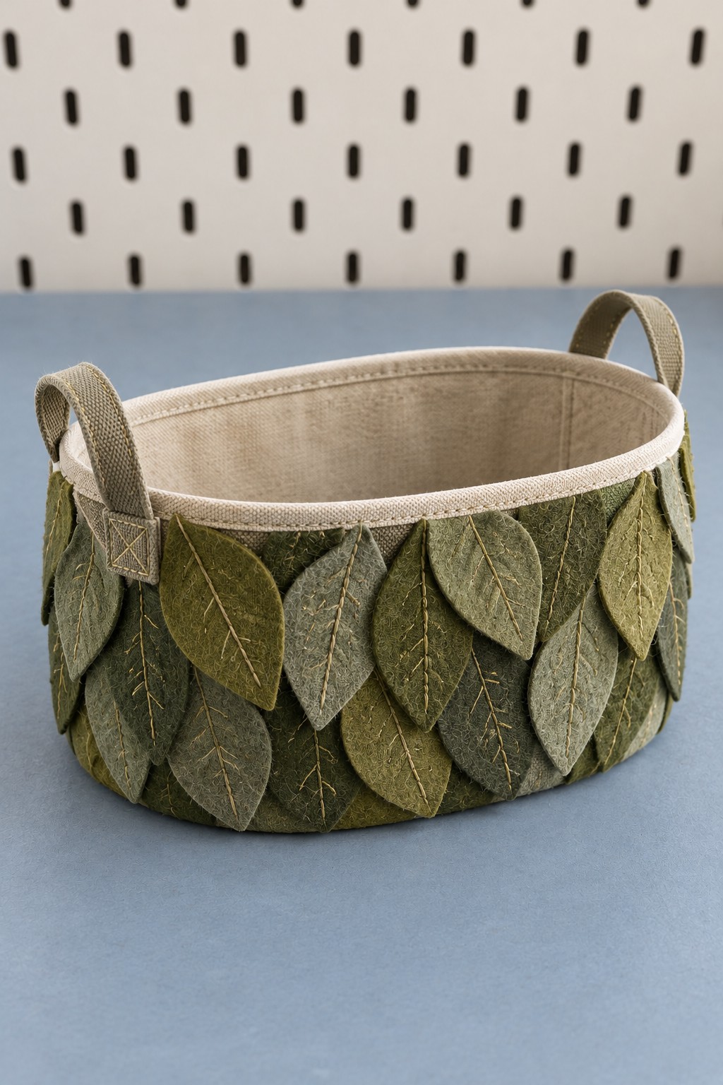 Oval fabric storage basket decorated with overlapping green leaves and two original handles