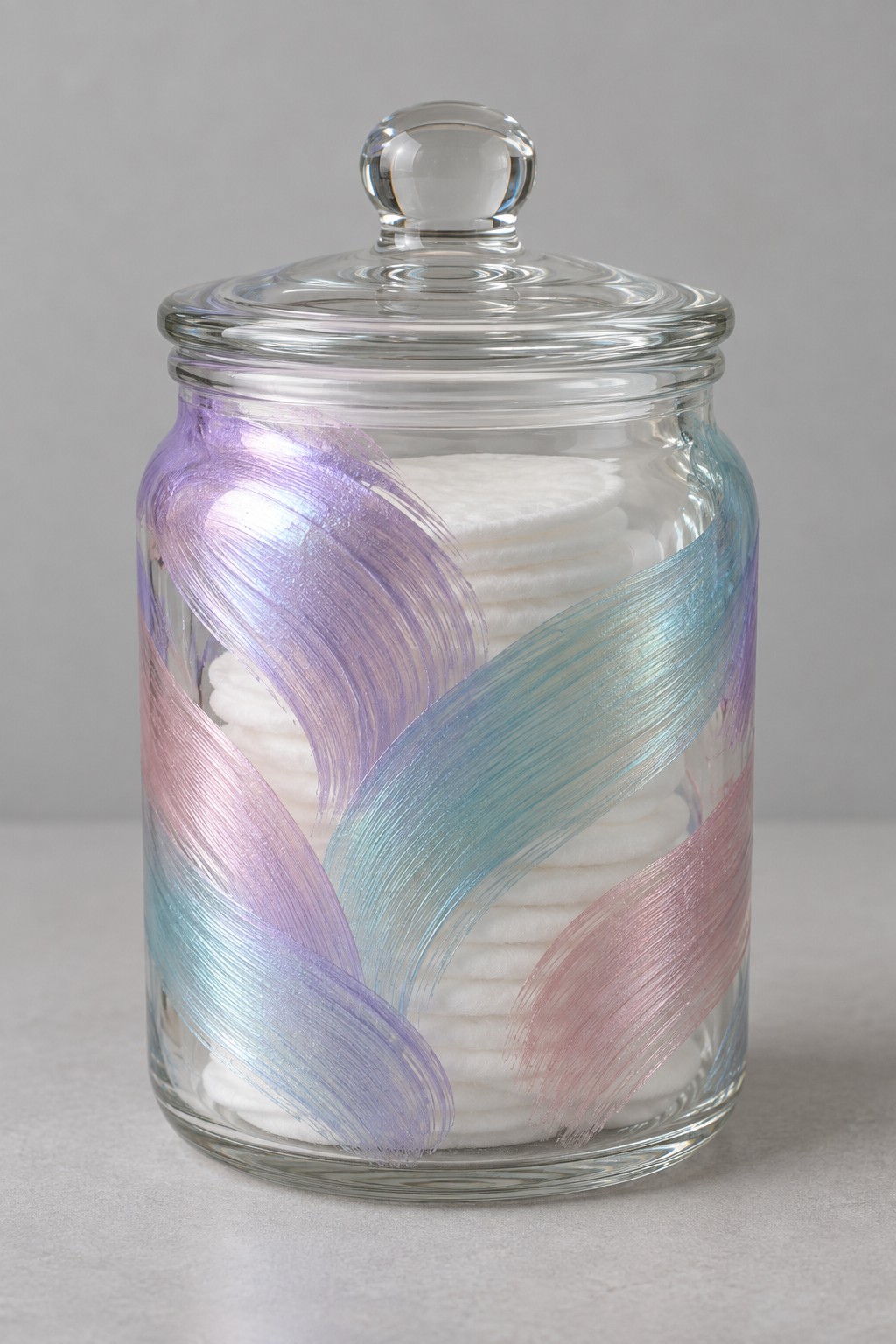 Clear lidded jar holding cotton pads with sweeping lavender blue and pink painted bands