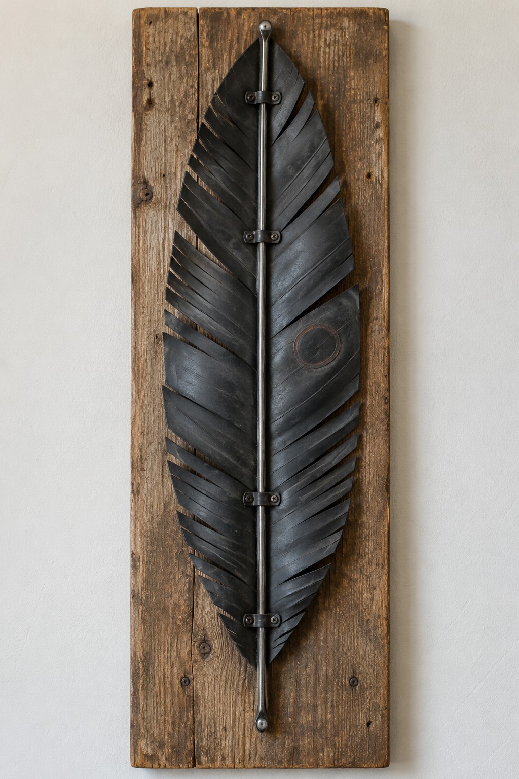 Large black feather sculpture with diagonal vanes secured beneath a metal spine on reclaimed wood