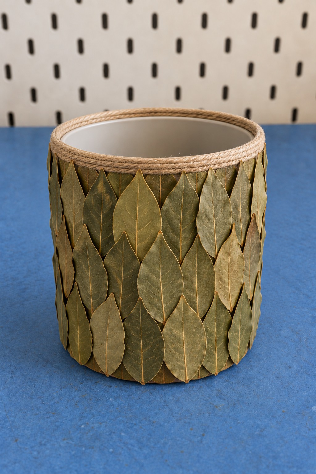 Cylindrical storage holder covered in vertical green leaves with jute around its upper rim