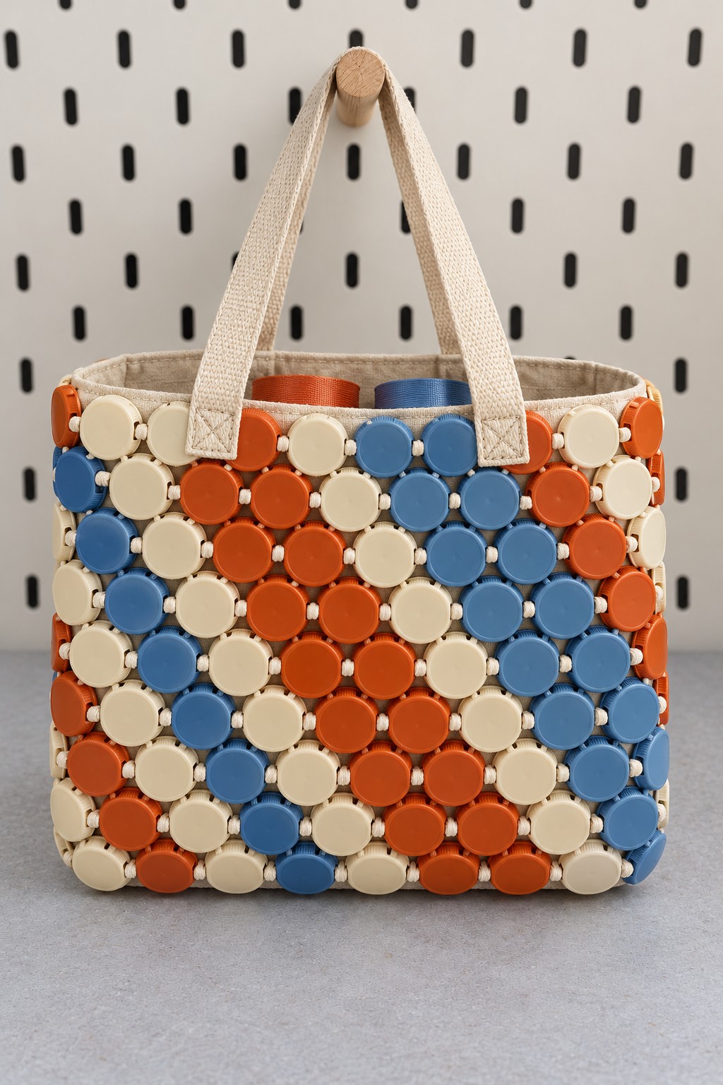 Cream, orange, and blue plastic bottle cap tote bag joined with cream cord and finished with canvas handles and lining