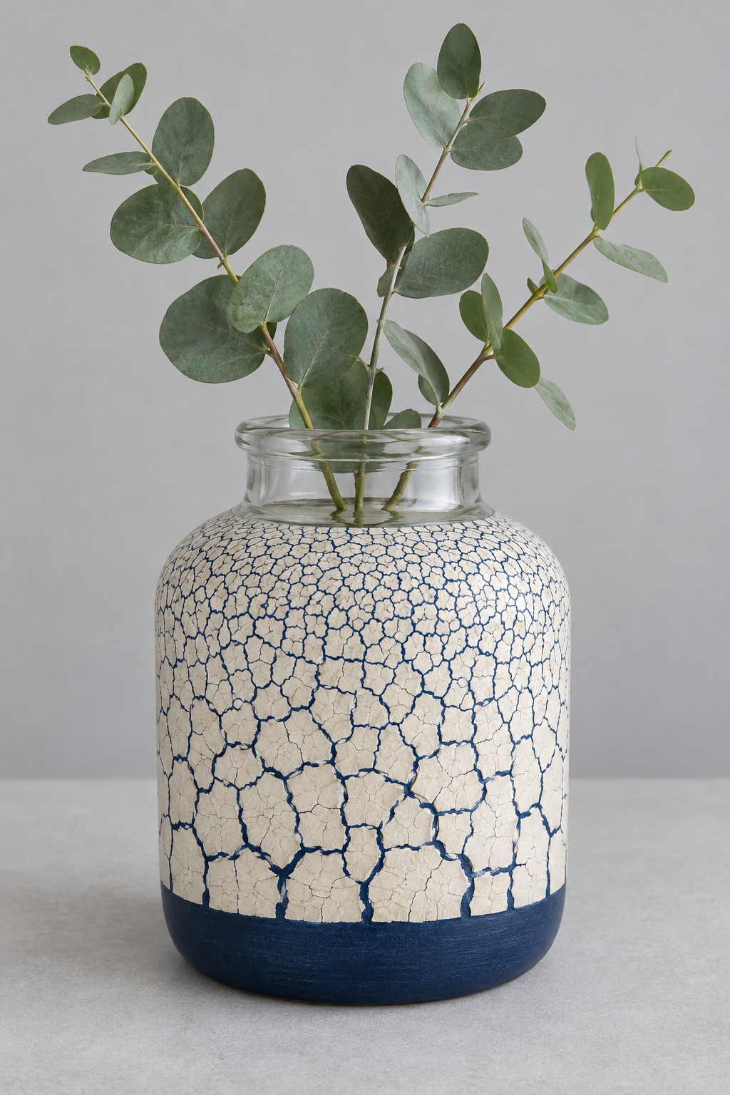 Rounded jar vase with a navy lower band and an ivory crackle effect exterior holding green stems
